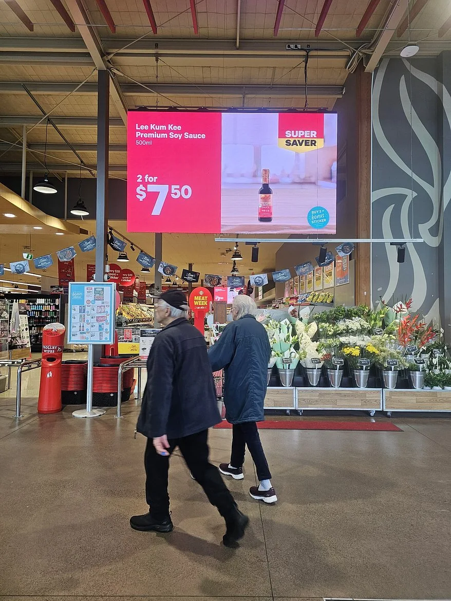 Customers passing a digital promotion display in a New World store